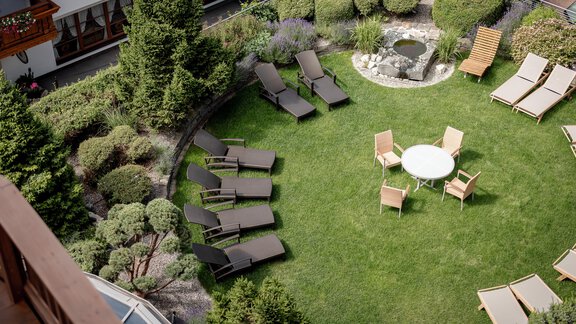 Ein ruhiger Garten mit Liegen und einem Tisch in der Mitte. Grüne Pflanzen umgeben die entspannende Atmosphäre. - Das Central - Alpine . Luxury . Life - Sölden