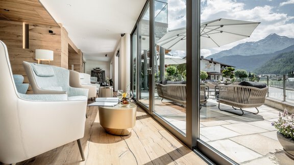 Ein modernes Wohnzimmer mit großen Fenstern und einem herrlichen Blick auf die Berge. Draußen befindet sich eine gemütliche Terrasse mit Sitzgelegenheiten und Sonnenschirm. - Das Central - Alpine . Luxury . Life - Sölden