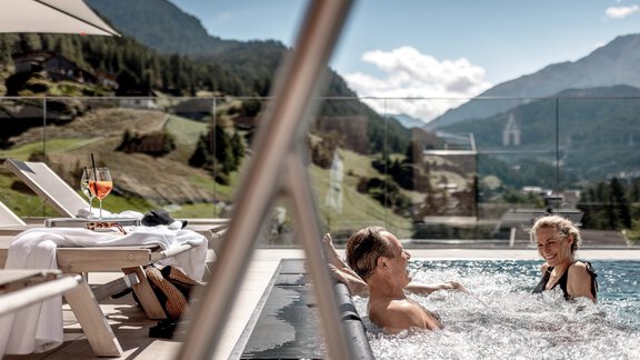 Ein Paar entspannt im Whirlpool mit Blick auf die Berge. Neben dem Pool stehen Liegen und ein Getränk. - Das Central - Alpine . Luxury . Life - Sölden