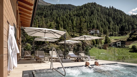 Ein entspannender Außenbereich mit einem Whirlpool und Liegen. Im Hintergrund sind grüne Berge und ein klarer Himmel zu sehen. - Das Central - Alpine . Luxury . Life - Sölden