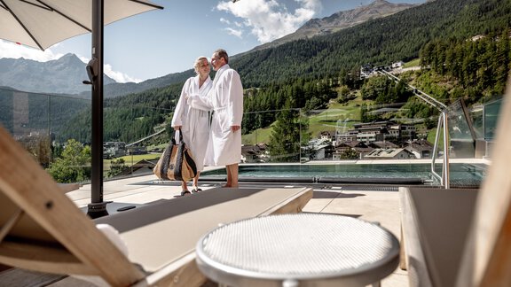 Ein Paar in Bademänteln steht am Pool mit Blick auf die Berge. Die Umgebung ist entspannt und luxuriös, ideal für einen Wellness-Tag. - Das Central - Alpine . Luxury . Life - Sölden