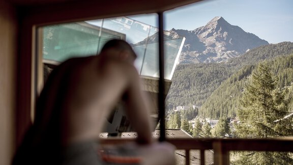 Ein Mann sitzt am Fenster mit Blick auf eine beeindruckende Berglandschaft. Die Natur um ihn herum ist grün und ruhig. - Das Central - Alpine . Luxury . Life - Sölden