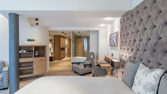 Ein modernes Schlafzimmer mit einem großen, gepolsterten Kopfteil und einem gemütlichen Stuhl. Der Raum ist hell und gut gestaltet, mit Holz- und Helltonakzenten. - Das Central - Alpine . Luxury . Life - Sölden