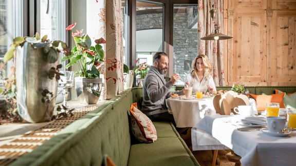 Ein gemütlicher Frühstücksraum mit einem grünen Sofa und einem Tisch, der mit Speisen und Getränken gedeckt ist. Zwei Personen sitzen entspannt und genießen ihre Mahlzeit. - Das Central - Alpine . Luxury . Life - Sölden