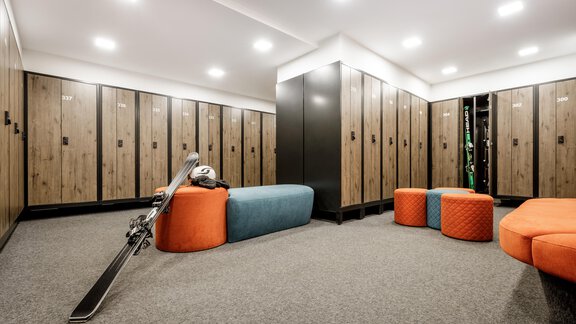 Ein moderner Umkleideraum mit Holzschränken und gemütlichen Sitzgelegenheiten. Skiausrüstung liegt neben den bunt gepolsterten Hockern. - Das Central - Alpine . Luxury . Life - Sölden