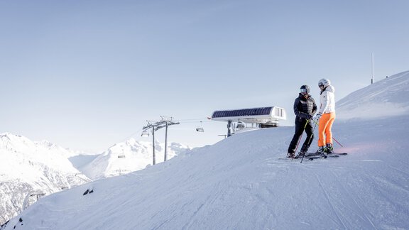 Zwei Skifahrer stehen auf einer verschneiten Piste mit Bergen im Hintergrund. Ein Skilift ist ebenfalls sichtbar. - Das Central - Alpine . Luxury . Life - Sölden