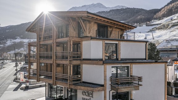 A modern wooden building in the mountains with a clear sky. The sun shines brightly on the facade of the hotel. - Edelweiss echt.charmant. - Sölden