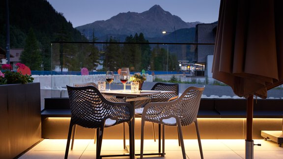 A cozy table with chairs on a terrace at twilight. In the background, mountains can be seen that create a relaxed atmosphere. - Edelweiss echt.charmant. - Sölden