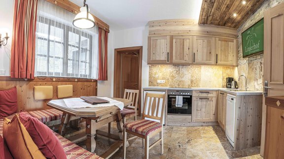 A cozy kitchen with a dining table and wooden chairs. The walls are in warm wood and earth tones, and there are large windows that let in plenty of light. - Ferienappartements Linserhof - Sölden