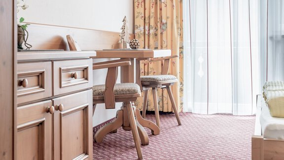 A cozy room with a wooden desk and two stools. Large windows with curtains let in plenty of light. - Ferienhaus Apart Sonnzeit - Sölden