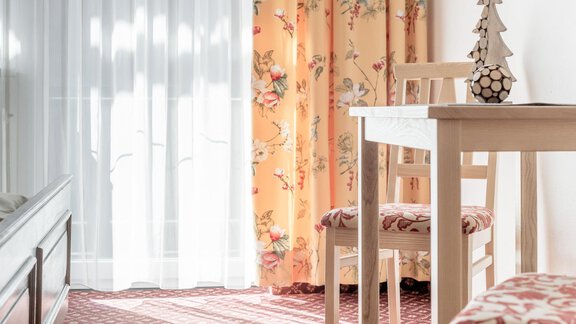 A friendly furnished room with a white table and chairs. The room has cozy curtains with a floral pattern and plenty of natural light. - Ferienhaus Apart Sonnzeit - Sölden