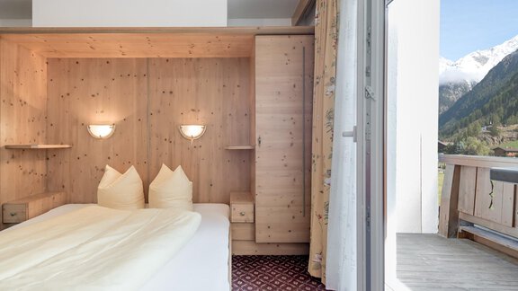 A cozy bedroom with wooden paneling and two beds. The view outside showcases mountains and a balcony. - Ferienhaus Apart Sonnzeit - Sölden
