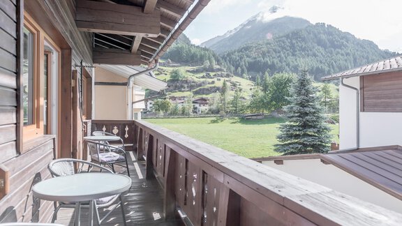 A balcony overlooking a green landscape and mountains. Two chairs and a table invite relaxation. - Ferienhaus Apart Sonnzeit - Sölden