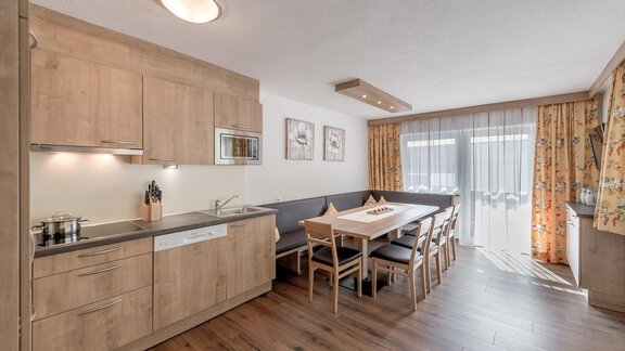 A modern kitchen with wooden cabinets and a dining area. The large window lets in plenty of light and offers a cozy view outside. - Ferienhaus Apart Sonnzeit - Sölden