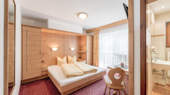 A cozy hotel room with a large bed and wooden furniture. The room is bright and friendly with a window that lets in daylight. - Ferienhaus Apart Sonnzeit - Sölden