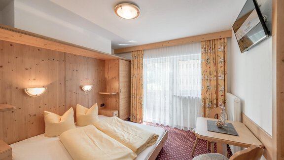 A cozy hotel room with paneling and two beds. The room has a window with curtains and a small desk. - Ferienhaus Apart Sonnzeit - Sölden