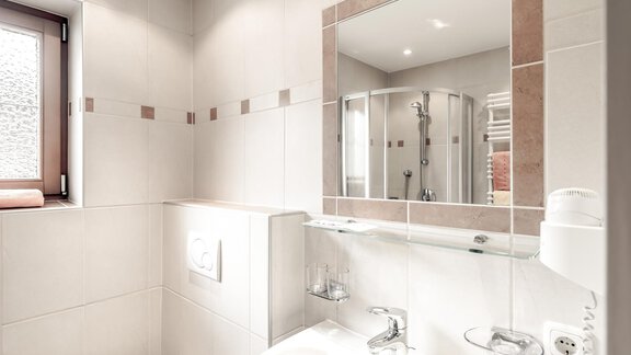 A modern bathroom with a bright tiled floor and a large mirror. The shower is separate, and a window provides daylight. - Ferienhaus Apart Sonnzeit - Sölden