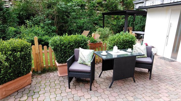 A cozy garden seating area with two chairs and a table. Surrounded by lush greenery and white flowers. - Ferienhaus F2 - Sölden - Sölden
