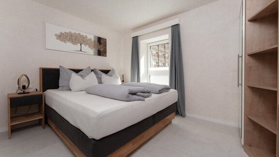 A modern bedroom with a large bed and soft padded pillows. The walls are bright, and a window with curtains provides natural light. - Ferienhaus F2 - Sölden - Sölden
