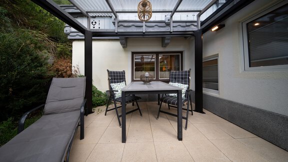 A cozy courtyard with a table and chairs under a covered area. In the background, green plants can be seen. - Ferienhaus F2 - Sölden - Sölden
