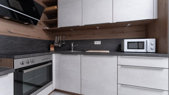 A modern kitchen with light cabinets and a dark work area. There is a stove, a sink, and a microwave. - Ferienhaus F2 - Sölden - Sölden