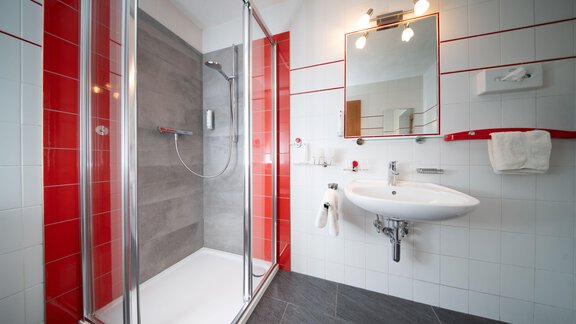 A modern bathroom with a glass shower and gray tiles. The walls are decorated with white and red tiles. - Ferienhaus F2 - Sölden - Sölden