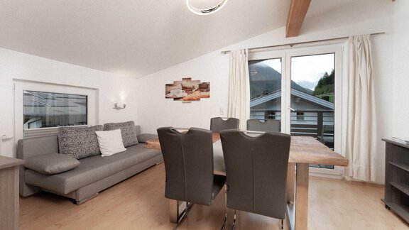 A modern living room with an elegant dining table and a comfortable couch. Large windows provide a view of the outdoors and plenty of natural light. - Ferienhaus F2 - Sölden - Sölden