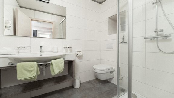 A modern bathroom with a shower, sink, and toilet. Green towel holder and large mirrors create a bright atmosphere. - Ferienhaus F2 - Sölden - Sölden