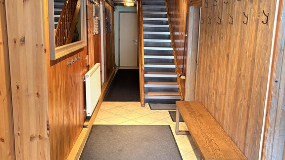 An inviting hallway with wooden paneling and a staircase. On the sides are hooks for jackets and a large mirror. - Ferienhaus Kaspers - Sölden