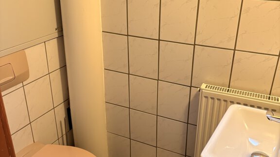 A small bathroom with a pink toilet and a sink. The walls are tiled and a window provides light. - Ferienhaus Kaspers - Sölden