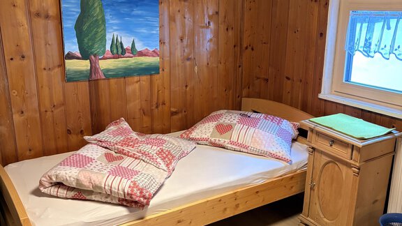 A simple bedroom with a wooden bed and pillows. A picture hangs on the wall and there is a small cabinet next to the bed. - Ferienhaus Kaspers - Sölden