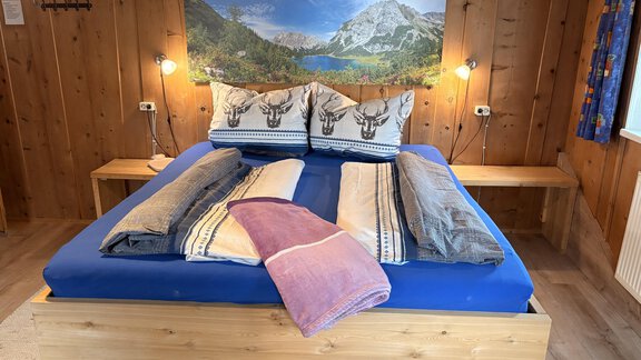 A cozy bedroom with a large bed and wooden decor. In the background hangs a beautiful landscape painting. - Ferienhaus Kaspers - Sölden