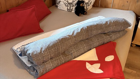 A cozy bed with red cushions and a gray blanket. On top lie two more blankets in red and white. - Ferienhaus Kaspers - Sölden