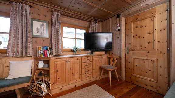 A cozy room with wooden paneling, a television, and windows that let in natural light. The decor is simple and inviting. - Ferienhaus Valsora - Sölden