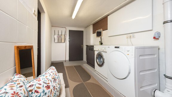 A modernly furnished laundry room with washing machine and dryer. The room features a cozy seating area and bright wall colors. - Ferienhaus Valsora - Sölden