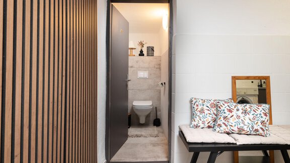 A bright entrance area with a door to a bathroom. Decorative cushions lie on a bench and a mirror stands next to it. - Ferienhaus Valsora - Sölden