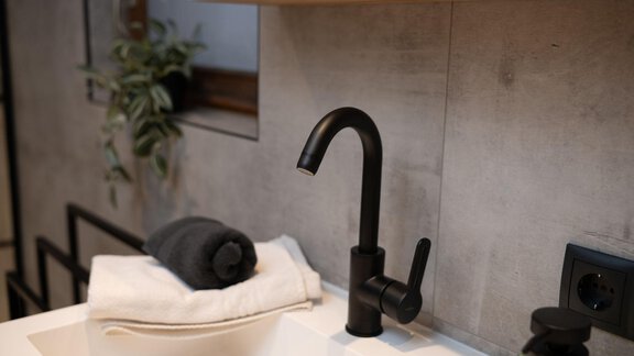 A modern bathroom with an elegant black faucet and a towel. In the background, a green plant is visible. - Ferienhaus Valsora - Sölden