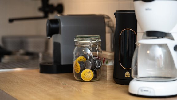 A modern kitchen with various kitchen appliances. On the countertop, there is a glass with coffee capsules and a coffee machine. - Ferienhaus Valsora - Sölden