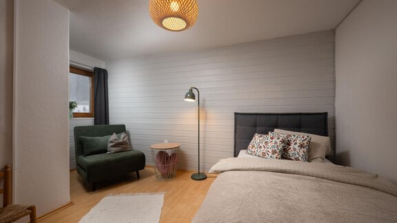 A cozy bedroom with a bed, a floor lamp, and a sofa. The walls are bright, and the room is well lit. - Ferienhaus Valsora - Sölden