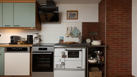 A modern kitchen with gray and green cabinets. On the countertop are coffee and kitchen appliances as well as a wall made of bricks. - Ferienhaus Valsora - Sölden