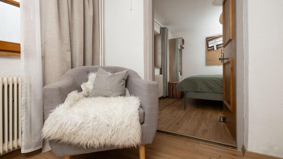 A cozy armchair with a soft cover is in a bright room. In the background, you can see a bedroom with a bed. - Ferienhaus Valsora - Sölden