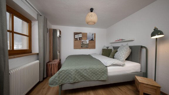 A cozy bedroom with a bed and green bedding. There is a window, a chair, and simple lighting. - Ferienhaus Valsora - Sölden