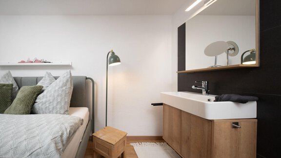 A modern bedroom with a bed, a wooden dresser, and a large mirror. A floor lamp complements the elegant decor. - Ferienhaus Valsora - Sölden