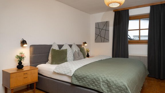 A modern bedroom with a large double bed and cozy bedding. A decorative picture hangs on the wall, and the window lets in daylight. - Ferienhaus Valsora - Sölden