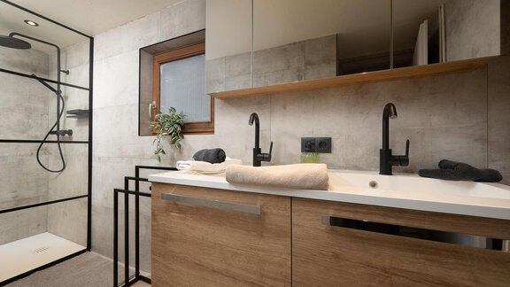 A modern bathroom with a glass shower cabin and an elegant wooden sink. Large mirrors and minimalist fixtures create a stylish look. - Ferienhaus Valsora - Sölden