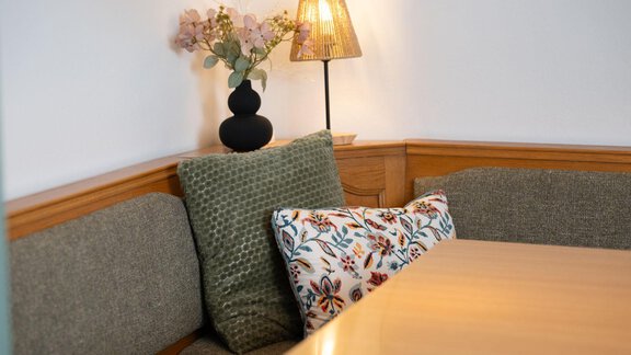 A cozy seating area with a wooden table and several cushions. On the table, there is a lamp and a floral arrangement. - Ferienhaus Valsora - Sölden