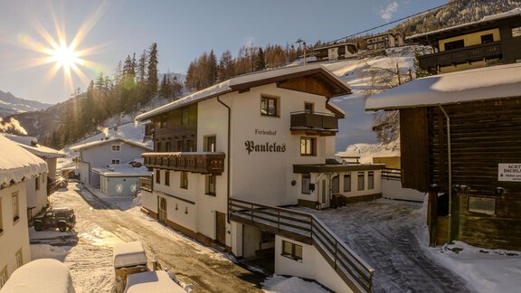 A picturesque winter village with snow-covered houses. The sun shines over the mountains, giving the scene a warm atmosphere. - Ferienhof Paulelas - Sölden