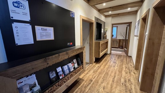 A bright corridor with wooden panels and an information board. On the wall, signs and brochures are available for guests. - Franzele Appartements & Zimmer - Sölden