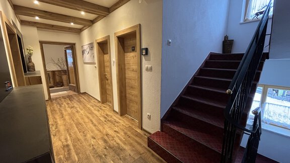 A bright hallway with warm wooden floors and modern doors. To the right, a staircase leads up, while natural light pours through the windows. - Franzele Appartements & Zimmer - Sölden