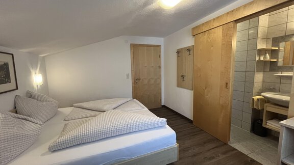 A cozy room with a double bed and wooden details. There is an adjoining bathroom with modern tiles. - Franzele Appartements & Zimmer - Sölden